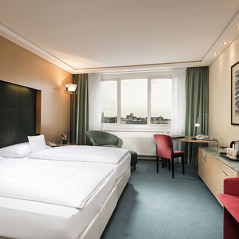 Comfort Zimmer im Maritim proArte Hotel Berlin mit Doppelbett, Schreibtisch, Sessel und Ausblick auf die Stadt.