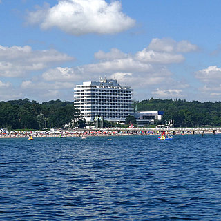 Maritim Seehotel Timmendorfer Strand, Seebrücke und bunte Flaggen vom Boot aus bei sonnigem Wetter.