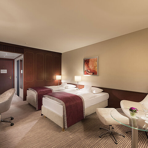 Comfort Zimmer im Maritim Hotel Bonn, ausgestattet mit zwei Einzelbetten, Sessel, Schreibtisch und moderner Beleuchtung.