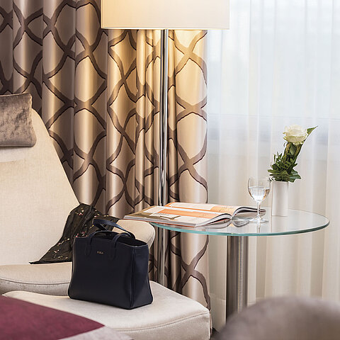 Detail eines Classic Zimmers im Maritim Hotel Bonn mit gemütlichem Sessel, Vorhang, Tisch, Glas, Rose und einer Tasche.