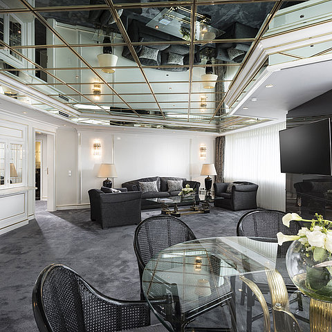 Stilvolles Wohnzimmer der Luxus-Suite im Maritim Hotel Bonn mit Spiegeldecke, modernen Möbeln und einem großen Esstisch.