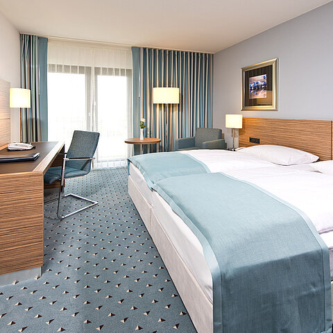 Comfort Zimmer im Maritim Hotel Darmstadt mit modernem Design, Schreibtisch, Sitzbereich und Blick auf große Fenster.