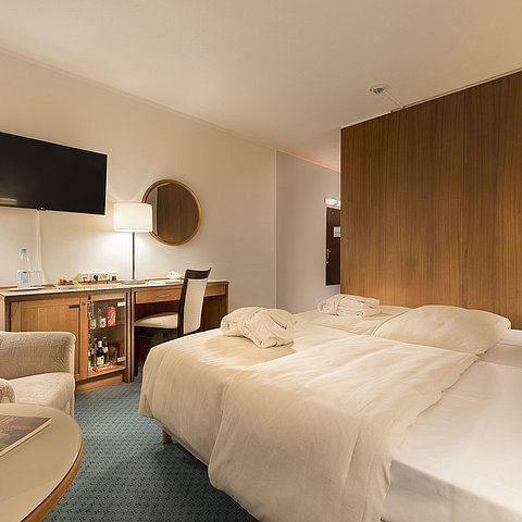 Classic Zimmer im Maritim Seehotel Timmendorfer Strand mit zwei Betten, Minibar, Schreibtisch, TV und Sitzgelegenheit.