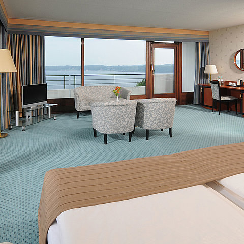 Junior Suite im Maritim Hotel Kiel, mit Sitzecke, Schreibtisch, TV und großer Fensterfront mit Meerblick.