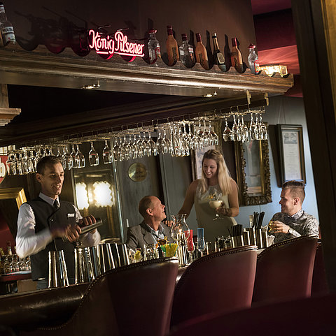 Stimmungsvolle Bar im Maritim Hotel Kiel mit Gästen, die Cocktails genießen, während der Barkeeper einen Drink mixt.