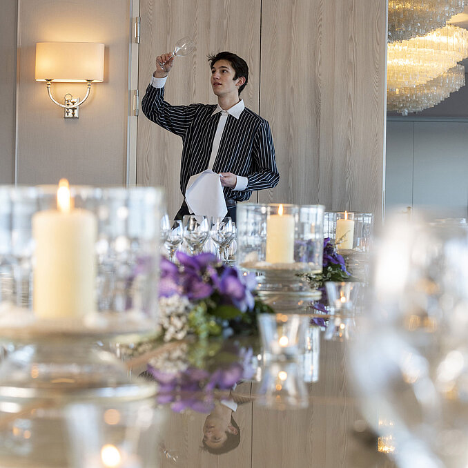 Mitarbeiter im Salon Oslo im Maritim Hotel Kiel prüft ein Weinglas, festlich gedeckter Tisch mit Kerzen und Blumendekoration.