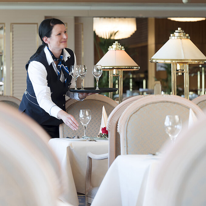 Kellnerin deckt einen Tisch im Restaurant des Maritim Hotels Timmendorfer Strand, mit eleganter Atmosphäre und Glaslampen.