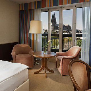 Superior-Zimmer im Maritim Hotel Köln mit Sitzbereich, komfortablem Bett und Blick auf den Kölner Dom.