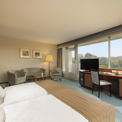 Comfort Zimmer im Maritim Hotel Kiel mit gemütlicher Sitzecke, Schreibtisch, großem Bett und herrlichem Blick ins Grüne.