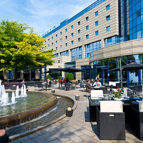 Terrasse des Maritim Hotels Bonn mit Sitzbereichen, Springbrunnen und Gästen, die im Freien speisen und entspannen.
