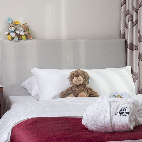 Familiensuite im Maritim Hotel Bonn mit einem gemütlichen Bett, Kuscheltieren und Bademantel, perfekt für Kinder.