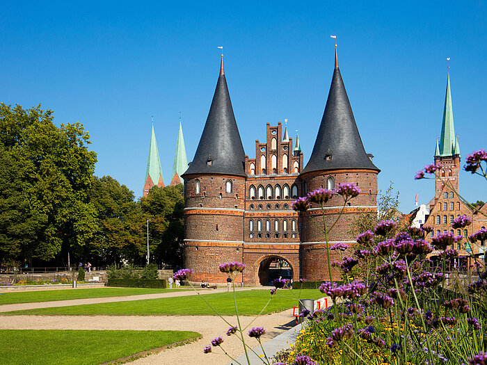 Holstentor in Lübeck mit blühenden Blumen im Vordergrund und blauem Himmel.