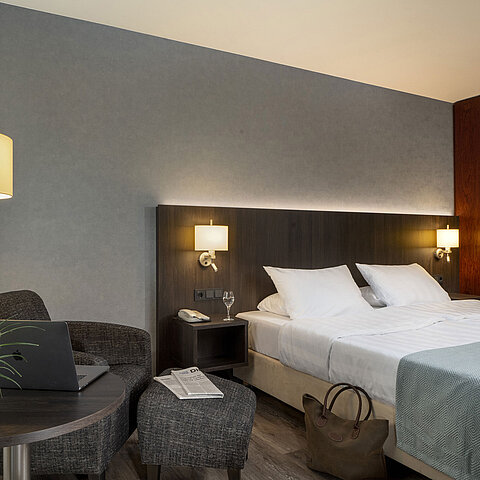 Modernes Doppelzimmer im Maritim Hotel Bremen mit gemütlicher Sitzecke, Beistelltisch, Vase und einladendem Bett.