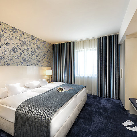 Elegante Suite im Maritim Hotel Bonn mit einem großen Bett, blauer Bettdecke und stilvollem Dekor.