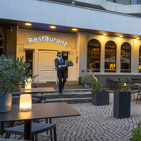 Abendstimmung auf der Terrasse des Maritim Hotels Darmstadt mit einem Mitarbeiter, der ein Tablett zum Restaurant trägt.