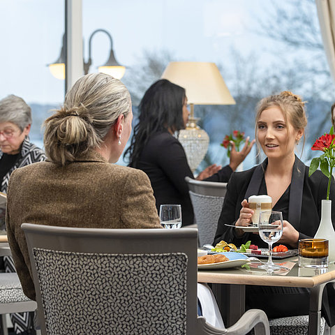 Gäste im Restaurant Bellevue im Maritim Hotel Kiel, entspannte Gespräche bei Getränken und Speisen mit Blick auf das Meer.
