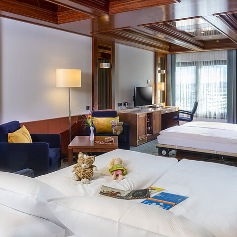 Familienzimmer im Maritim Hotel Darmstadt mit Spielzeug auf dem Bett,einem Schreibtisch mit TV und einer gemütlichen Sitzecke