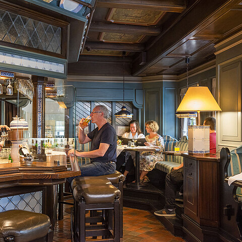 Gemütliche Hotelbar im traditionellen Stil mit Gästen, die Getränke genießen, und einem Barkeeper, der Bier zapft.