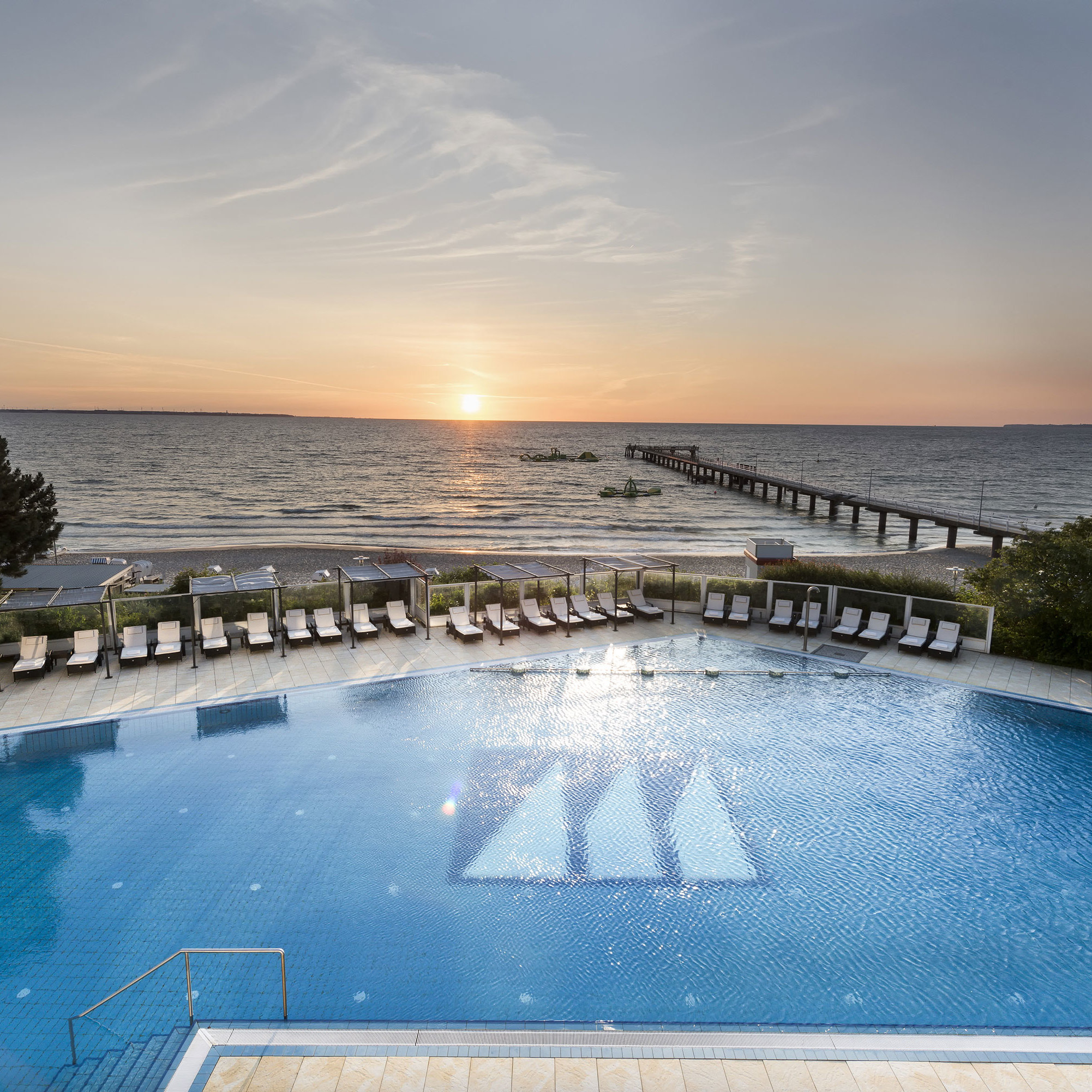 Pool mit Meerblick im Maritim Seehotel Timmendorfer Strand bei Sonnenuntergang, Liegen und Steg am Strand.