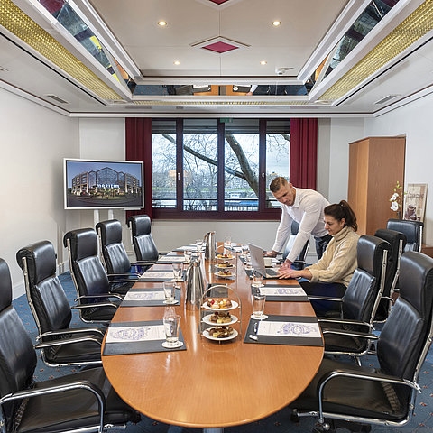 Zwei Personen arbeiten im Salon Boardroom des Maritim Köln mit Laptops an einem Besprechungstisch mit Getränken und Snacks.