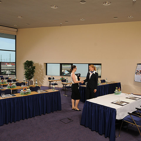 Heller Tagungsraum im Maritim Hotel Dresden mit gedeckten Tischen, Flipchart und zwei Personen beim Händeschütteln.
