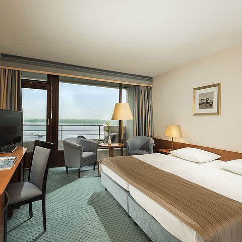Superior Zimmer im Maritim Hotel Kiel mit Schreibtisch, Sitzbereich, großem Doppelbett und Balkon mit Blick auf die Förde.
