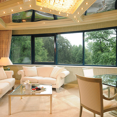 Luxuriöse Junior Suite im Maritim Bremen mit eleganter Sitzecke, Glas-Esstisch und großem Panoramafenster mit Blick ins Grüne