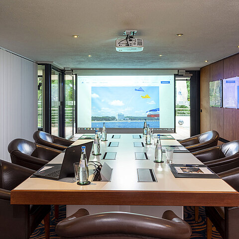 Konferenzraum „Salon Fulda“ im Maritim Hotel Timmendorfer Strand mit Konferenztisch, Ledersesseln und Projektor.