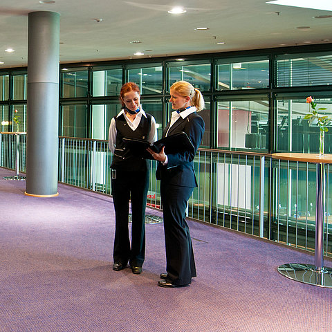  Foyer im Maritim Hotel Dresden mit zwei Mitarbeitenden in Uniform, Stehtischen und einer Obststation.