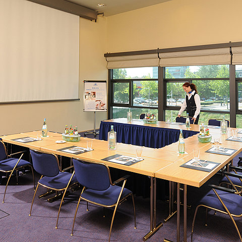 Tagungsraum im Maritim Hotel Dresden mit U-förmiger Tischanordnung, Präsentationsleinwand und Vorbereitungen für ein Meeting.