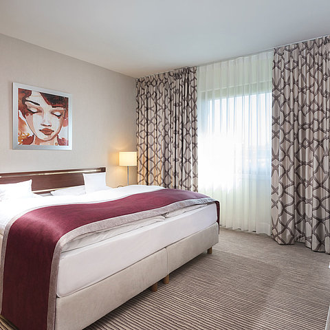 Geräumige Suite im Maritim Hotel Bonn mit gemütlichem Doppelbett, moderner Einrichtung und weinrotem Bettläufer.